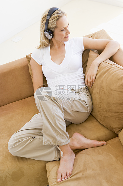 在客厅里听耳机笑着说话的女人微笑长椅家庭座位椅子休息室女子音乐技术设备图片