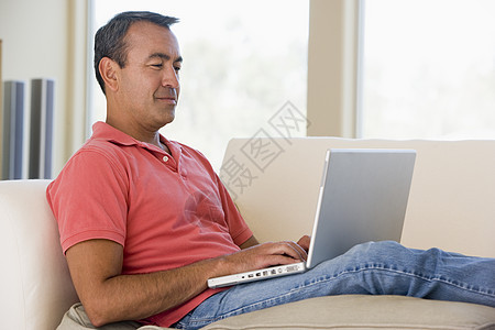 使用笔记本电脑和微笑在客厅里的人水平家庭互联网混血长度男性中年上网沙发成人图片