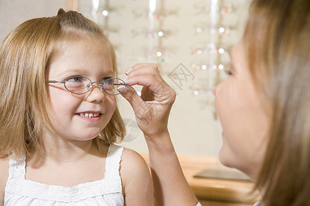 妇女用眼镜对着在观光家微笑的年轻女孩试戴眼睛眼镜帮助商业妈妈中年夫妻验光师保健母亲水平女性图片