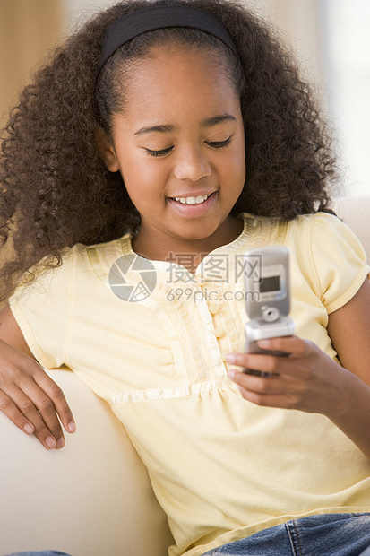 使用手机和微笑在客厅的年轻女孩女性短信长椅细胞椅子技术电话孩子家庭沙发图片