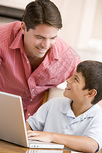 男人笑着用笔记本电脑在厨房帮助小男孩家长孩子们冲浪微笑家庭作业儿子桌子技术男性两个人图片