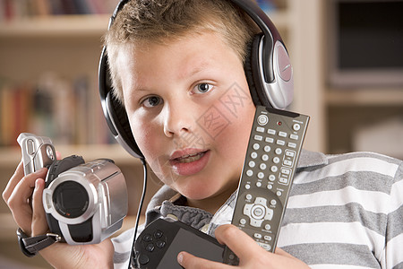 年轻男孩在卧室里戴耳机 手持许多电子设备头肩水平视频一个男孩游戏孩子们录影机娱乐孩子图片