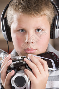 年轻男孩在卧室里戴耳机 手持许多电子设备电话孩子电子游戏水平工具一个男孩视频录影机技术图片