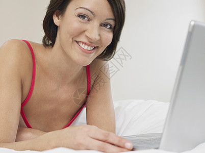 床铺上使用笔记本电脑的妇女图片