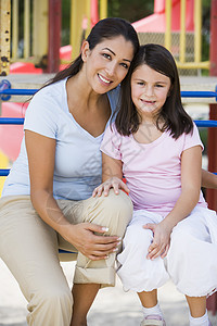母亲和女儿女孩坐在操场结构上微笑的笑容图片