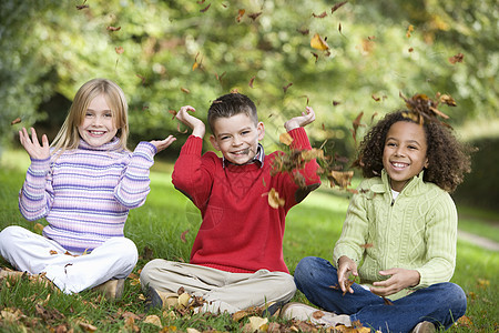 三名儿童坐在户外公园中微笑着笑容的小孩爸爸父亲们成年人孩子们孩子落叶叶子家庭外表情感图片