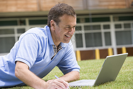 男人用笔记本电脑躺在学校草坪上服饰衣服教育夜校成年人成人情感服装教育性大学图片