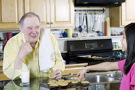 老年男子与孙女分享曲奇饼孩子巧克力片烘烤厨房男人混血牛奶房子微笑零食图片