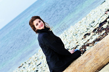 女孩在海滩上的女孩青少年女性套衫原木海洋天空帽子库存木材蓝色图片