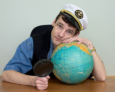 身着制服帽的男子与地球拥抱男生头饰地球仪帽子玻璃放大镜蓝色桌子男人图片