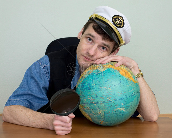 身着制服帽的男子与地球拥抱男生头饰地球仪帽子玻璃放大镜蓝色桌子男人图片