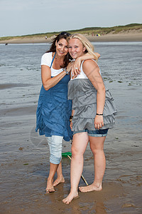 母亲和女儿一起女士假期女性金发阳光微笑拥抱黑发海滩女性化背景图片