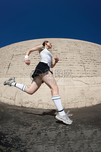 女人向终点线冲刺马尾辫白色女性力量赛跑者臂带砖墙建筑圆形阴影图片