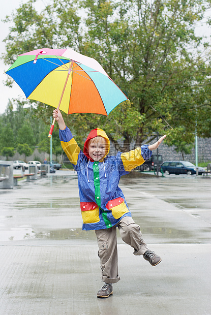 带着雨伞的男孩站在雨下微笑男生防水童年表情雨衣乐趣水池俏皮男性图片