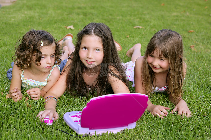 三个小女孩在草地上玩玩具电脑游戏女性女孩们乐趣家庭朋友们工作电脑学生公园喜悦图片