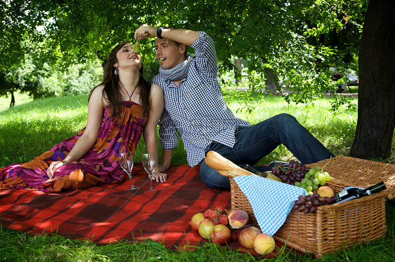 在男朋友喂养时坐在野餐毯子上吃饭的年轻夫妇图片