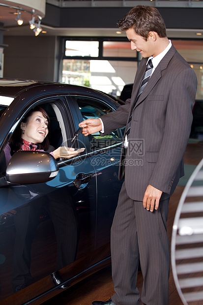 汽车推销员把车钥匙给一个年轻女人头肩中心销售员女性幸福代理商外表顾客男士后视镜图片