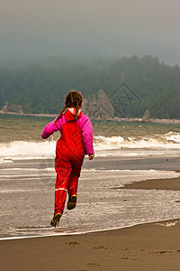 身着红雨衣的年轻女孩在美国瓦辛顿海滨红色青年乐趣孩子女儿靴子雨具海滩姐姐图片