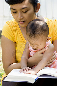 年轻母亲在照看婴儿时看书图片