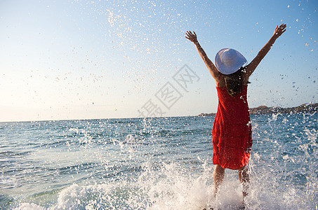 美丽的女孩在海浪中飘荡石头假期乐趣太阳日落裙子享受热带气候海滩图片