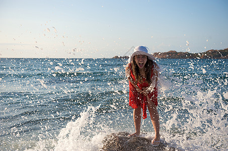 美丽的女孩在海浪中飘荡自由女性幸福海滩太阳日落帽子乐趣岩石气候图片