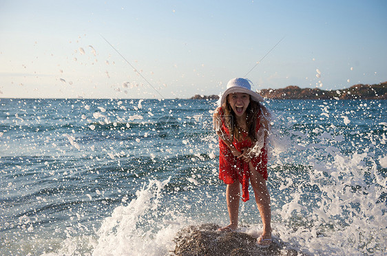 美丽的女孩在海浪中飘荡自由女性幸福海滩太阳日落帽子乐趣岩石气候图片