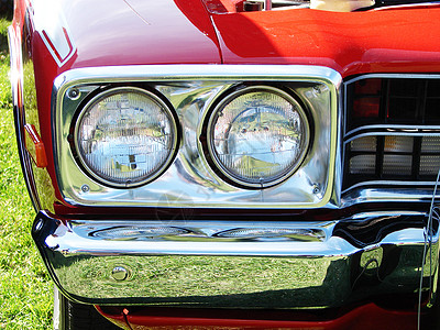 一辆明亮红色肌肉车的头灯和铬保险杠图片