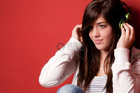 年轻女孩在红墙上用耳机监听音乐青少年乐趣享受黑发音乐播放器微笑娱乐女性闲暇女士图片