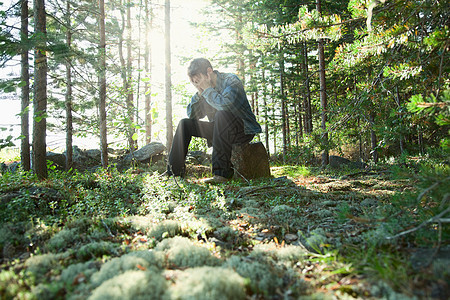 悲哀的年轻人坐在石头上的木头上图片
