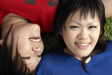 两个快乐的亚洲少女 躺在草地肖像上 穿着红蓝衣服幸福乐趣微笑红色说谎青少年女孩们图片