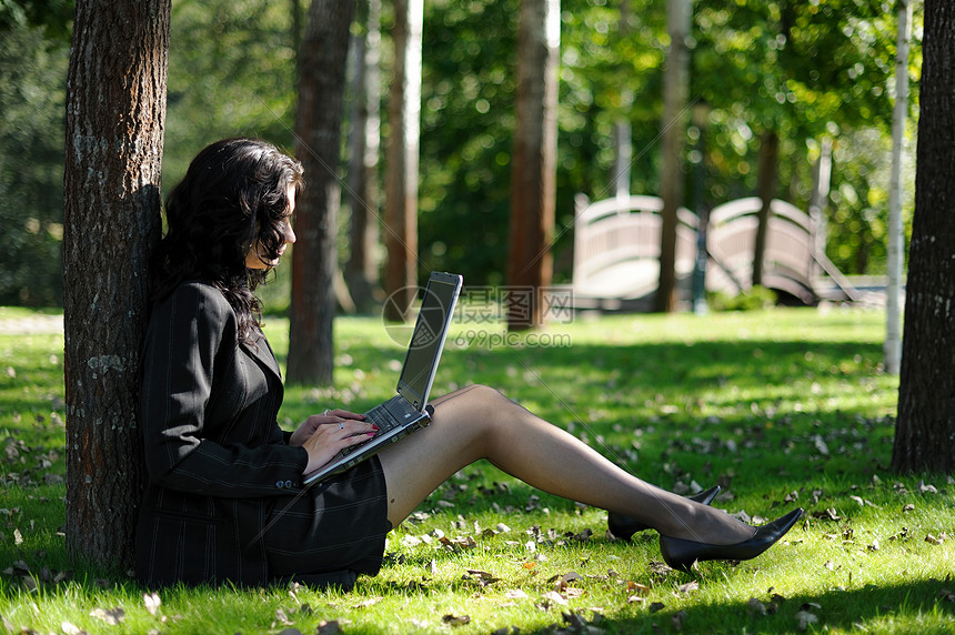 在公园里拿着笔记本的年轻女士成人移动头发人士上网商务互联网机动性树叶系统图片
