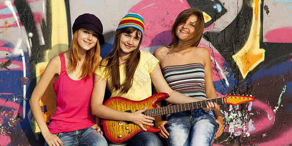 三个美丽的女孩 带着吉他和涂鸦墙 在背角青年闺蜜街道女士朋友们音乐女性城市乐趣喜悦图片