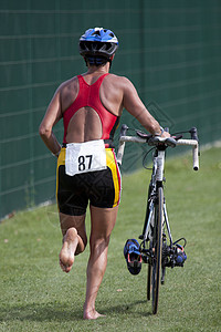 Triathlete推着他的自行车黑色把手运动员红色踏板腰带太阳过渡竞赛跑步图片