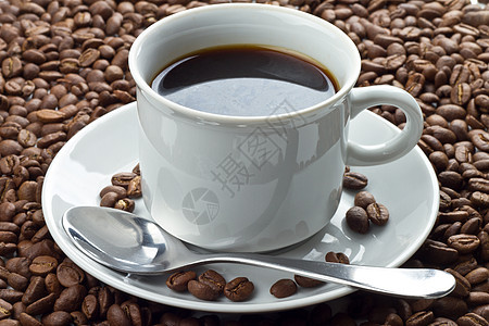 咖啡豆和白杯中的咖啡豆 放在汤匙的茶碟上图片
