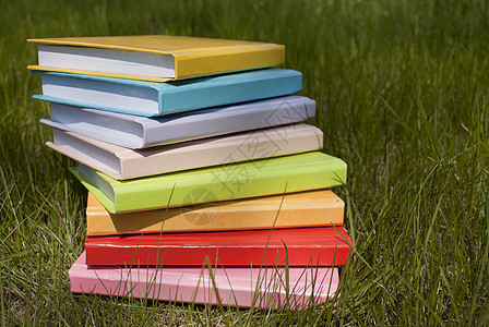 堆在草地上的书白色脊柱文学橙子黄色红色补给品团体绿色知识图片