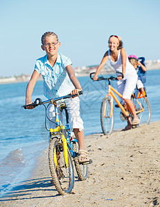 可爱的女孩和她的母亲和兄弟一起骑自行车孩子闲暇儿子蓝色青少年喜悦波浪女性公园海洋图片
