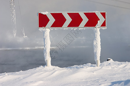 冰冻和下雪的向导路标志 在水上雾的背景中转弯图片