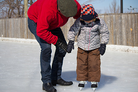 父亲教儿子如何滑冰平衡晴天两个人帮助冬装时间溜冰场教学爸爸家庭图片