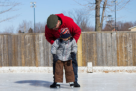 父亲教儿子如何滑冰男性冬装播放父母爸爸帮助两个人平衡溜冰场家庭图片