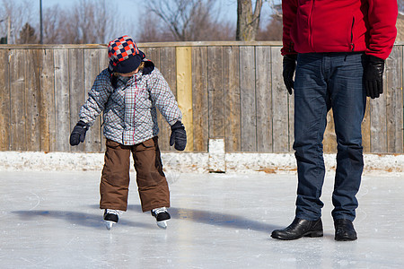 父亲教儿子如何滑冰男性学习溜冰场平衡家庭孩子晴天帮助男生冬装图片
