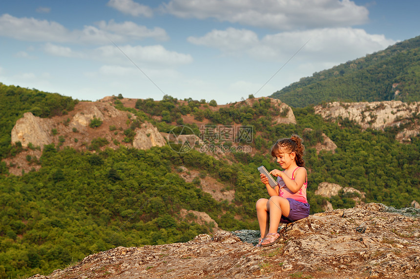 小女孩坐在山顶上玩平板牌的游戏图片