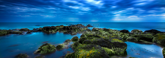 蓝色蓝海的黄昏笼罩着海洋和阴云天空火山日落木材海浪绿色岩石日出苔藓黑色图片