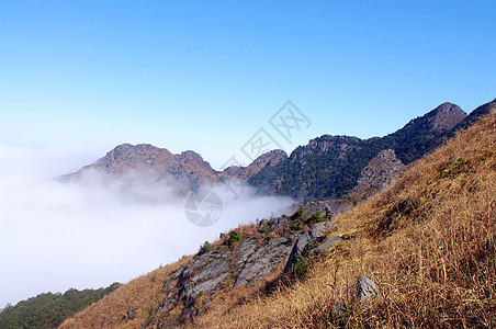 高山的山坡周围有云山顶山腰杂草游客天空登山者登山旅行稻草顶峰图片