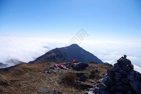 高山的山坡周围有云游客岩石羽绒被青金石天空太阳山腰登山登山者悬崖峭壁图片