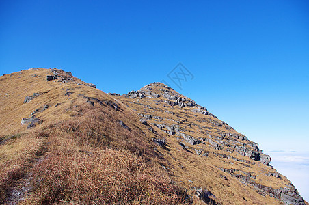 高山顶顶有岩石和草地高地羽绒被稻草风景天空多云杂草太阳登山者旅行图片