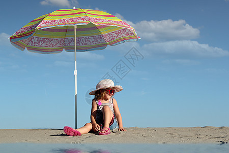 有太阳眼镜的小女孩 坐在阳光罩下帽子遮阳棚童年女性太阳镜青年海滩假期蓝色白色图片