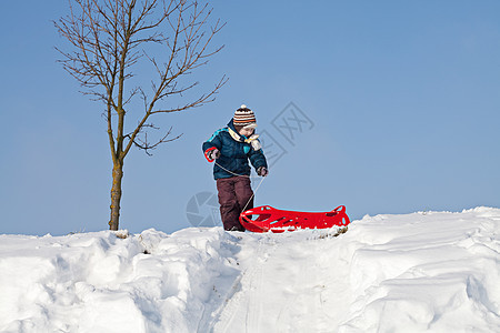 男孩把红色塑料雪橇拉到雪山上图片