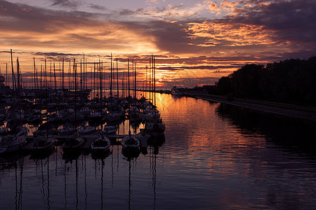 以日落时的游艇为港湾光束帆船戏剧性橙子海岸冒险反射海洋码头桅杆图片