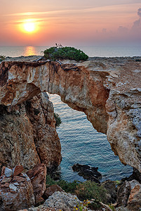 海岸线上空的石形拱门海浪支撑悬崖日落海景波浪阳光太阳洞穴海洋图片