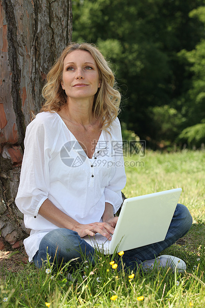 女人用电脑坐在草地上图片